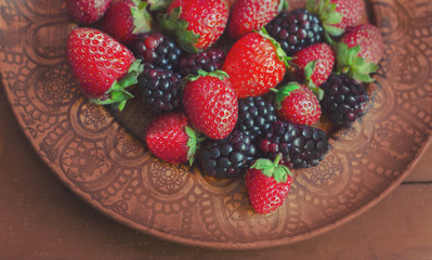 Blackberries and strawberries on a clay plate .