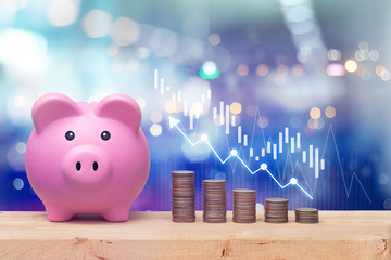 Pink piggy bank and coins stack on wooden table with candlestick chart suitable for finance and...