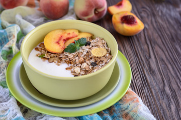 Useful breakfast of muesli with peach slices is in a bowl on a wooden table