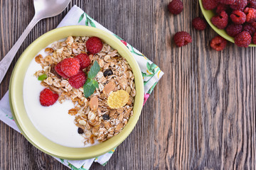 Useful breakfast of muesli with raspberries is in a bowl on a wooden table