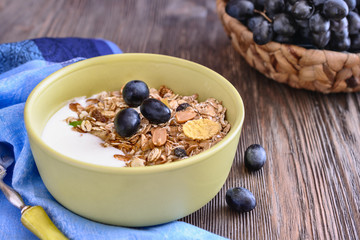 Useful breakfast of muesli with grapes is in a bowl on a wooden table
