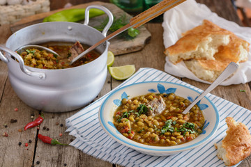 Delicious country soup from a mixture of legumes in a plate next to aluminum saucepan with soup is...