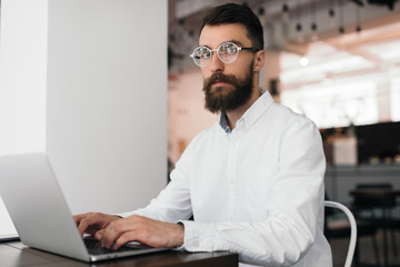 Handsome bearded journalist using laptop computer working project, creating blog publication, edition text at workplace. Portrait of successful good-looking businessman typing on keyboard in office. 