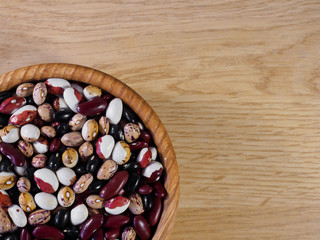 Colored beans in a plate. Colored beans in a wooden plate on a textured wooden background. Vegetarian food. 