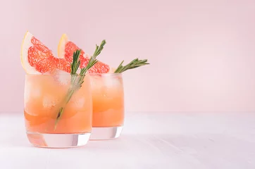 Abwaschbare Fototapete Cocktail Kalter Sommercocktail mit Eiswürfeln, Saft und Grapefruitscheiben auf pastellrosa Hintergrund.