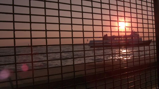 Ship in background at sunset seen through fence slow motion