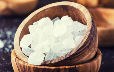 White crystal candy sugar in wooden bowl on black table, selective focus