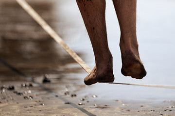 Man legs walk along a tight line in the beach,balances on the slackline close up