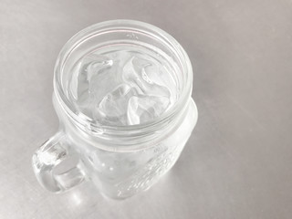 Glass of cool water with cube ice on gray table.