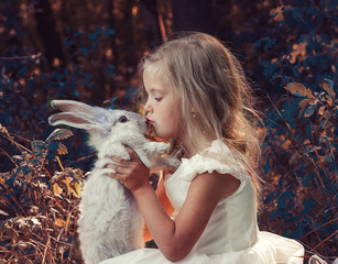 Маленькая девочка в белом платье сидит в лесу и держит в руках белого кролика. © inna717