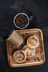 Curd fritters and takeaway coffee on a wooden serving tray, above view on a dark brown stone surface, vertical shot