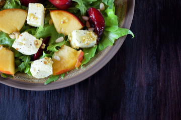 Fruit salad with arugula, plums, nectarines and soft cheese on a plate