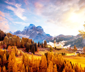 Amazing magical autumn unbeatable landscape with the church and  yellow larch on a background of mountains in the Dolomites in a sunny day near Codalonga, Alps, Italy.