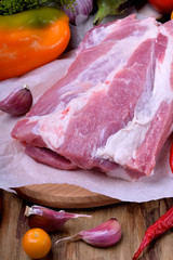 Piece of pork meat on a wooden cutting board surrounded by vegetables