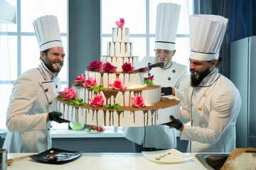 Three cooks are holding a huge cake