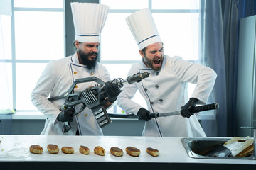 Two cooks in the kitchen with weapons in hand - obrazy, fototapety, plakaty