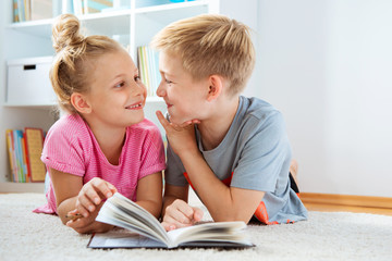 Portrait of two children reading a book on the floor at home