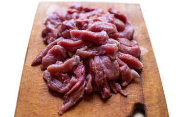 Sliced raw meat on a wooden board on a white background