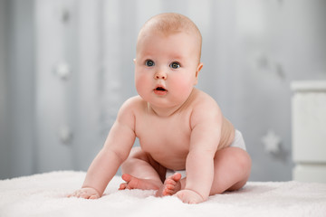 Naked baby in a diaper sits in a bright room