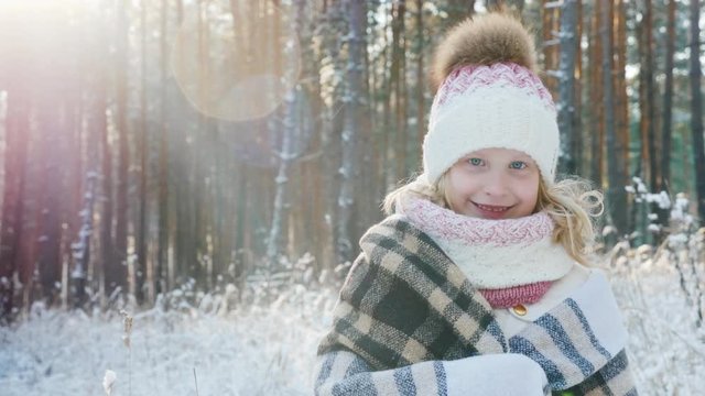 Portrait of a happy little girl wrapped in a plaid in a snow-covered winter forest