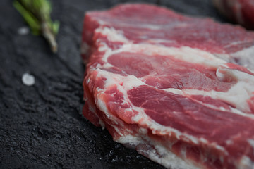 Fresh raw boneless pork neck slices on black stone background. Top view.