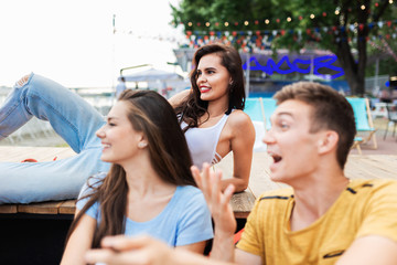 A company of good-looking friends laughing and socialising while sitting on the bench in the nice summer cafe. Cheers. Entertainment, having good time. Friendship.