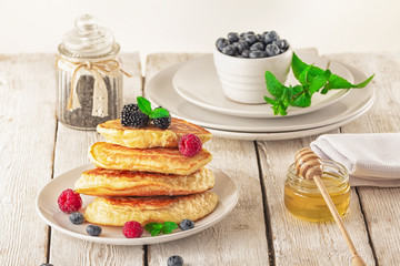 Pancakes with blueberries, honey and raspberry on a wooden background