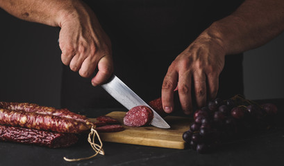 Men's hands cut sausage salami on a cutting board.