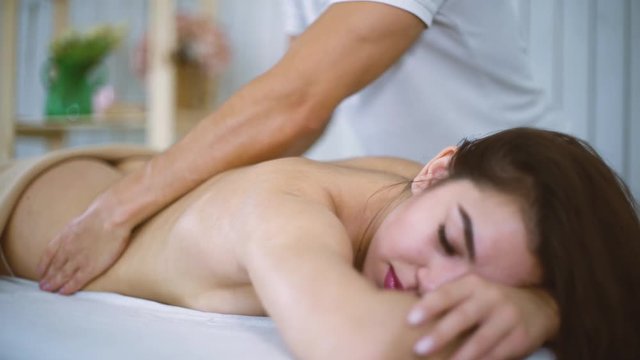 Male masseur hands massaging beautiful woman back in spa salon. Young female enjoying professional spine and back treatment. Rehabilitation, medicine, manual therapy, beauty, health and skin concept