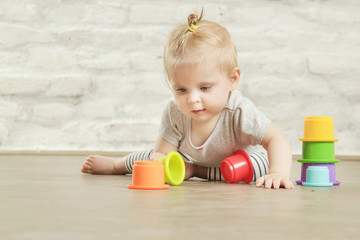 Baby girl playing on the floor with plastic educational cups, early learning concept