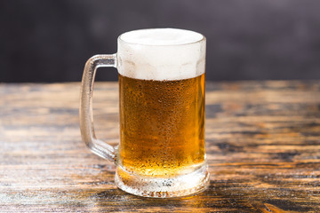 Cold glass of lager beer with foam and dew on wooden table
