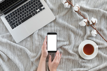 Cozy winter background with laptop, cup of hot tea with cotton branch, warm knitted blanket, vintage work space. Lifestyle concept