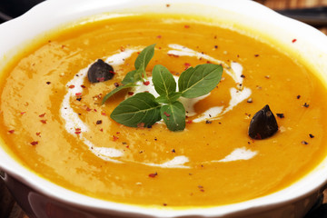 Roasted pumpkin and carrot soup with cream and pumpkin seeds on wooden background.