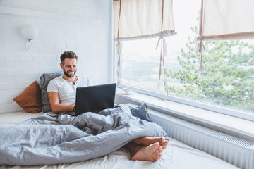 Man working in bed on laptop early in the morning - obrazy, fototapety, plakaty