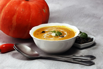 Roasted pumpkin and carrot soup with cream and pumpkin seeds on stone background.