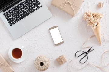 Fototapeta na wymiar Top view of woman workspace with laptop, beige flowers, smartphone on white textural background, flat lay. Stylish female blogger concept.