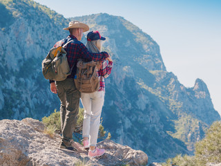 Man and woman backpackers standing and hugging on the mountain. Couple hikers with backpacks relaxing on top of a hill and enjoying sea view and cliffs.