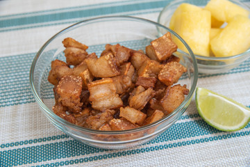 Transparent bowl with crackling, manioc and lemon on striped background