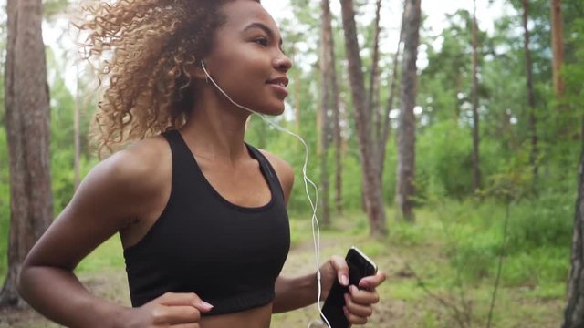 young beautiful African American woman with curly hair running with music in a forest, close up