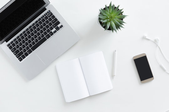 Top view of white office desk with laptop, green cactus and smartphone. Free space for text, business office flat lay concept