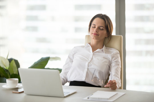 Young happy woman relaxing enjoying break feeling no stress free relief after computer work, meditating with eyes closed, resting leaning on comfortable ergonomic office chair breathing fresh air