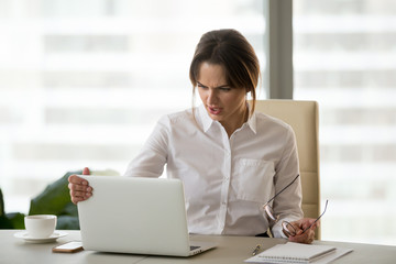 Confused angry businesswoman annoyed by laptop problem looking at screen of not working stuck computer, office employee feeling perplexed about spam email letter or disbelieving online news at work