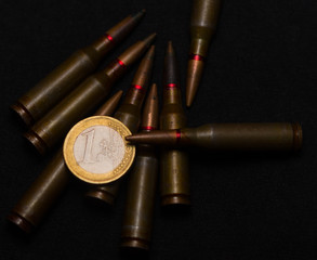 Rifle ammo around one euro coin on black background. Symbolizes the war for money and one of the world's problems.