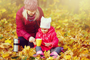 On an autumn walk Mom pours warm tea from her thermos to her daughters. The concept of a family...