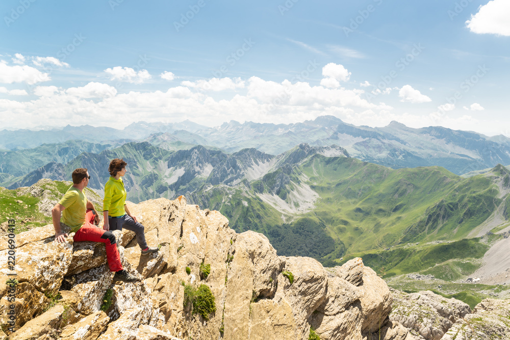 Wall mural pareja de montañeros en una cima rocosa mirando la impresionante paisaje montañoso.