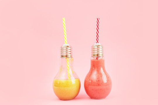 Two lamp- shaped jars with fruit smoothies isolated on pink background.