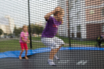 Defocused background of children on a trampoline. Grid in the foreground. Child Safety Concept