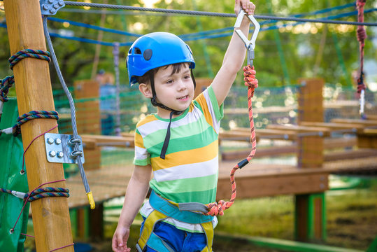 Little cute boy enjoying activity in a climbing adventure park on a summer sunny day. toddler climbing in a rope playground structure.