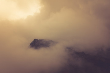 Fototapeta na wymiar View of morning fog in the mountains. Misty landscape of rocky mountain slopes. Color toning and low contrast. Outdoor travel background.