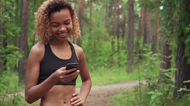young beautiful African American woman with curly hair is chatting in her phone before jogging